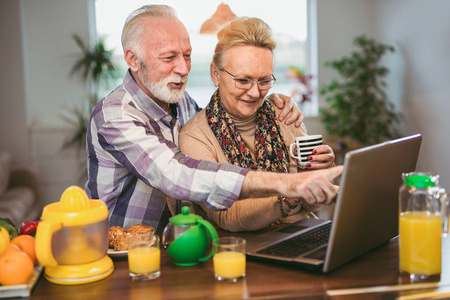 兴奋的看着一台笔记本电脑一起在厨房里指向和笑点有趣的在屏幕上的年长夫妇