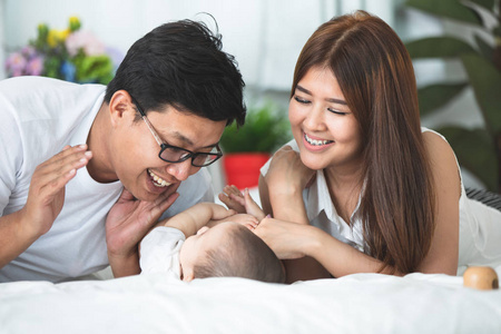 愉快的亚洲家庭父亲母亲与女儿玩在床上与微笑的面孔