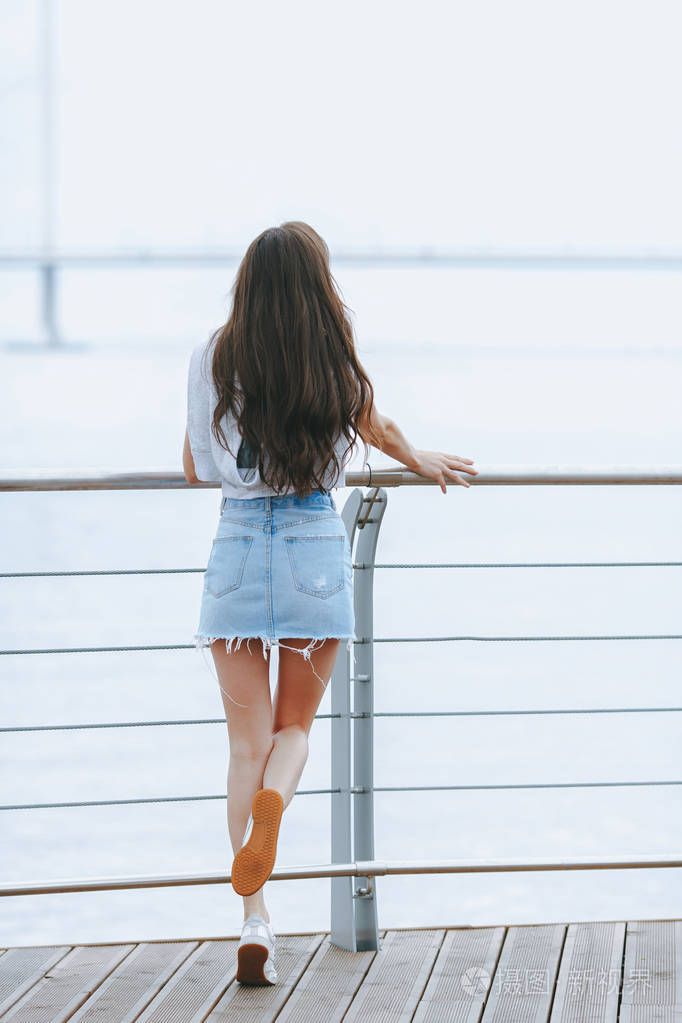 年轻迷人的女人站在她的背部在海滨长廊生活方式概念
