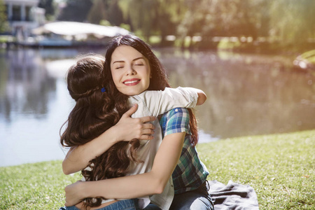 快乐的母亲和她的女儿坐在草地上.她正在拥抱孩子.