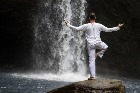 人站立在冥想瑜伽在岩石在瀑布