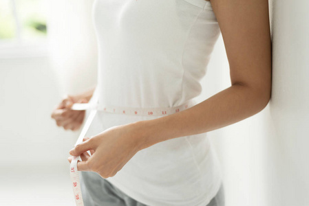 妇女在测量她的腰围与测量磁带在白色背景。健康的营养, 减肥, 苗条的身体, 健康的生活方式概念