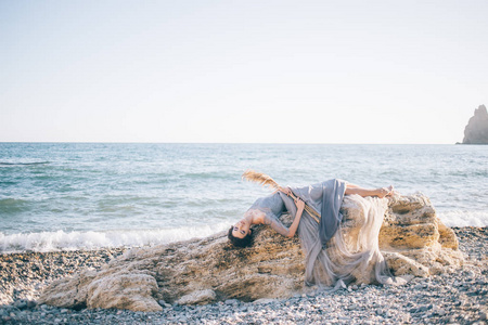 美丽的女人穿着一条长裙, 在海边的一块大石头上躺着。婚礼, 美术理念