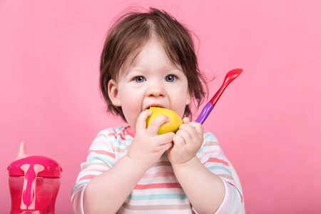 一个小女孩吃苹果坐在孩子的椅子上明亮的彩色浅粉色背景