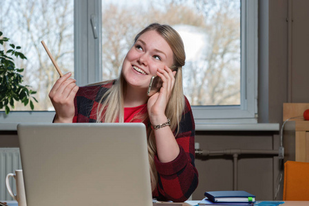 一个微笑的金发女郎坐在笔记本电脑上, 用手机聊天