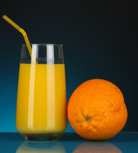 美味的橙汁在玻璃和它旁边暗蓝色背景上的橙色
