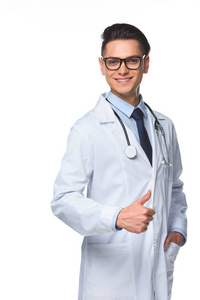 微笑的年轻医生显示拇指和看着在白色的相机隔离