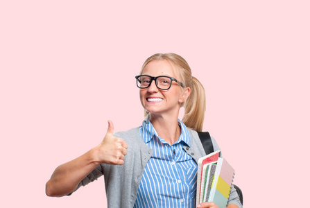 快乐的年轻学生女孩拿着书, 高中或大学 graduand 在粉红色的背景。返回学校
