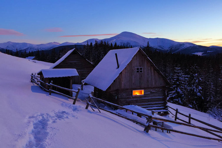 一条践踏的小路通向白雪覆盖的美丽雪山背景下的木屋。梦幻般的冬季风光