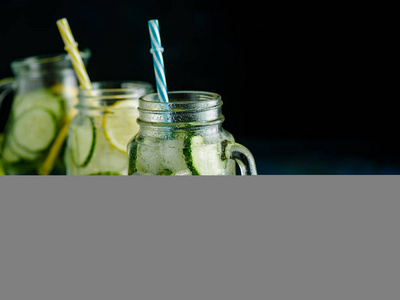 新鲜的夏日饮品。健康排毒汽水与柠檬和黄瓜在梅森罐子在黑暗的背景。健康食品概念。排毒饮食