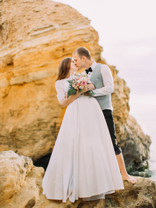 新郎的特写视图亲吻新娘与婚礼花束, 而站在悬崖上
