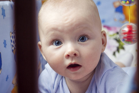 一个小婴儿的脸和蓝色的眼睛躺在她的肚子在婴儿床上