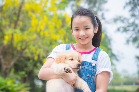 年轻的亚洲女孩在公园里捧着一只小金猎犬