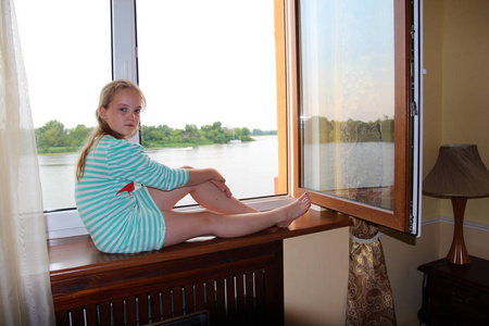 穿条纹连衣裙的少女坐在窗窗台附近打开的窗口, 并看着镜头照片