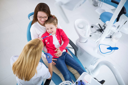 年轻女牙医显示女孩和她的母亲怎么洗牙