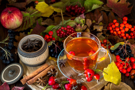 一杯热茶之间的秋天的落叶和木制背景上的浆果