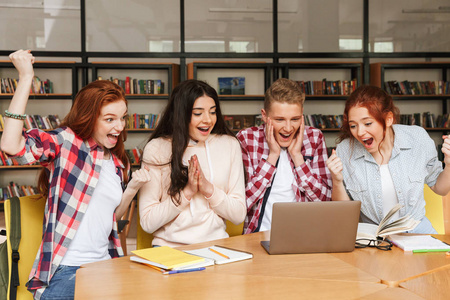 一群快乐的青少年做作业, 而坐在图书馆, 看着笔记本电脑屏幕