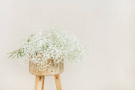 白色的满天星花花束在木凳上, 在苍白的粉彩米色背景。最小的生活方式概念