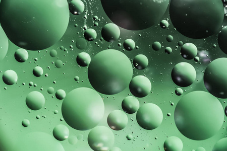油滴以圆和椭圆形的形式混乱位于水面, 暗宏绿色抽象背景照片
