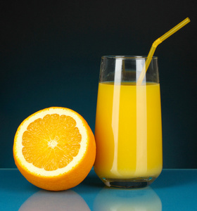 美味的橙汁在玻璃和它旁边暗蓝色背景上的橙色