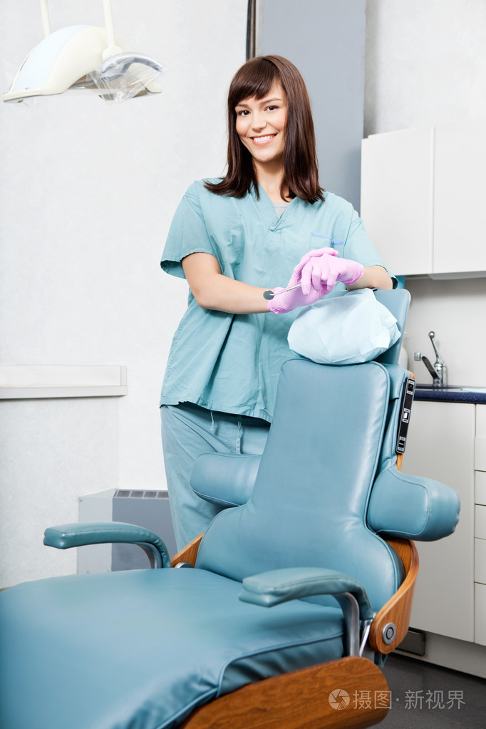 微笑着站在诊所牙科椅的女牙医
