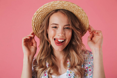 关闭一个可爱的年轻女子的肖像在夏季礼服和草帽看着相机孤立的粉红色背景
