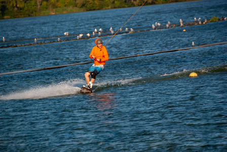 Wakeboarder, 在橙色的衬衫和头盔, 在一个阳光明媚的日子, 在一个有线公园的训练转弯。户外活动假期