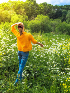 苗条的妇女旅行者在黄色夹克为在绿色的草之间散步