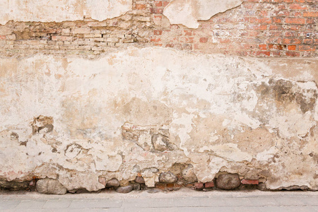 老风化老式砖墙破碎的石膏与地面上的路面.又脏又臭的城市背景照片