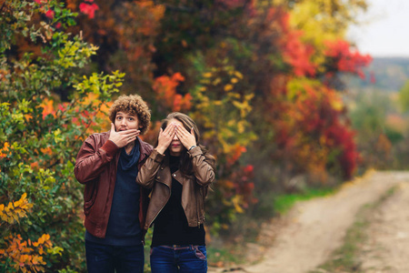 欢快的情侣表现出情感。男子和妇女在皮革夹克和牛仔裤显示的惊喜, 对秋季树木的背景
