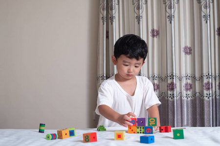 3岁的小可爱亚洲男孩玩玩具或方块拼图在家里的床上, 孩子躺在学习游戏块形状或片断, 教育和健康概念