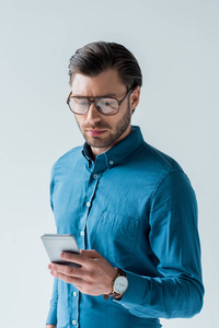 自信的年轻男子在时尚眼镜使用智能手机隔离白色