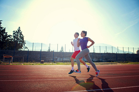 年轻的运动情侣在阳光明媚的日子在体育场跑道上慢跑