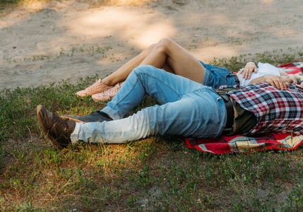 这家伙和那个女孩在夏天躺在草地上的格子格子上。穿着格子衫, 短裤和牛仔裤, 白色上衣