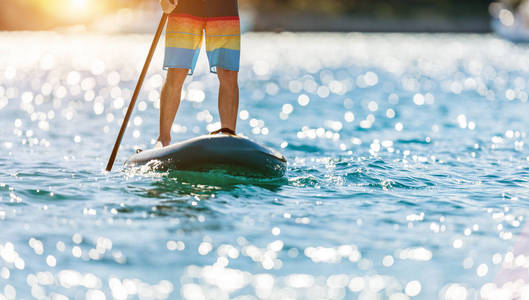 详细的年轻人站在 paddleboard。Paddleboarding 是现代交通与水活动的一种方式