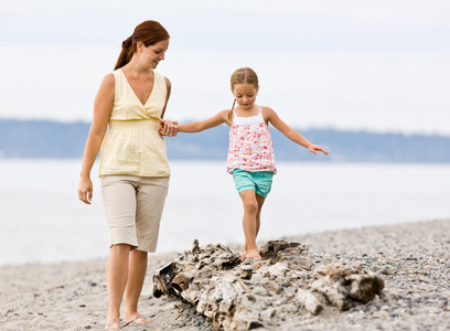母亲帮女儿在日志在海滩上走
