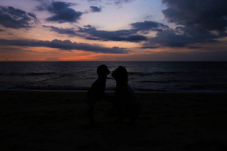 日落背景下海边母亲亲吻小女儿的剪影