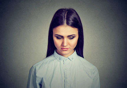 漂亮的黑发在衬衫向下看在沮丧的感觉不满与不幸的灰色背景照片