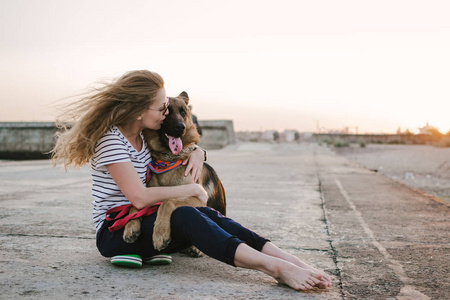 快乐的年轻女子抱抱她的德国牧羊犬户外在海上码头在日落期间