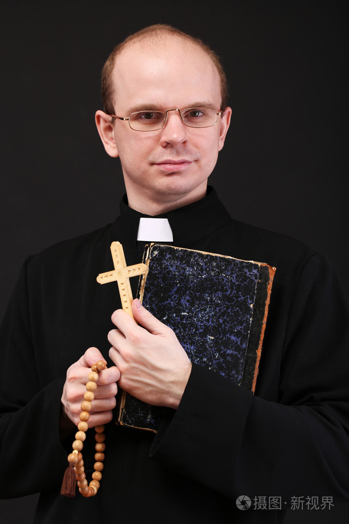年轻牧师与木制十字架和圣经,孤立在黑色