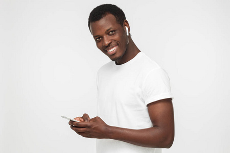 年轻的非洲裔美国男子看着和微笑着在相机与欢快的表情, 而短信他的朋友, 使用手机, 在灰色背景下隔离