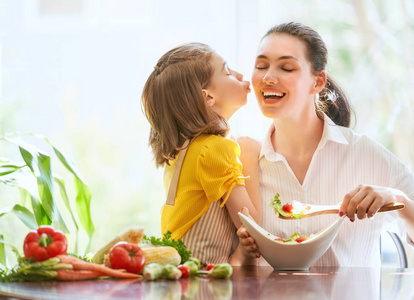 健康的食物在家里。幸福的家庭在厨房里。母亲和孩子的女儿正在准备蔬菜