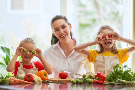 健康的食物在家里。幸福的家庭在厨房里。母亲和孩子的女儿们正在准备蔬菜。