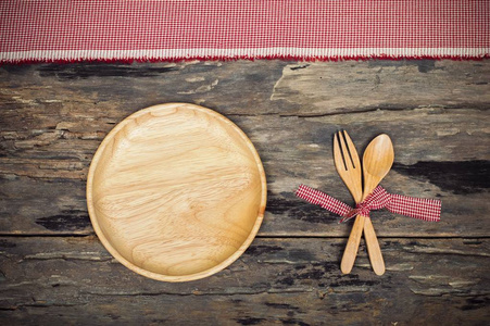 厨具。木制叉子, 勺子和菜在老木背景红色织品