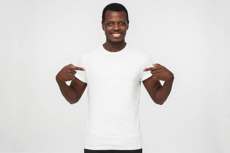微笑尼斯非洲裔美国人的男子指着白色 t恤与两个食指, 复制空间为您的广告, 孤立的灰色背景
