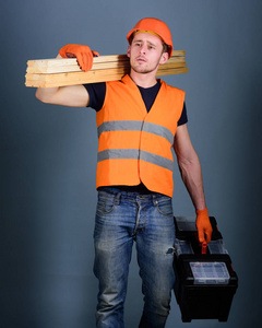 男子, 修理工在头盔, 硬帽子持有工具箱和木梁, 灰色背景。木匠, 木工, 劳动者, 建设者在梦幻般的脸上扛着木梁。木工理念