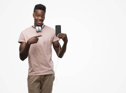 年轻的非洲裔美国人戴着耳机和手持智能手机非常高兴地指着手和手指
