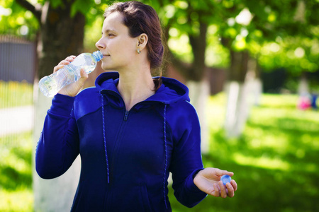 棕褐色的女孩在绿色的夏日公园喝瓶装水。健康的生活方式。饮用清洁水概念