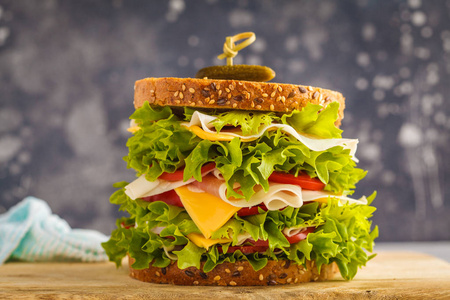大三明治与肉, 乳酪和新鲜的蔬菜在木板, 黑暗的背景