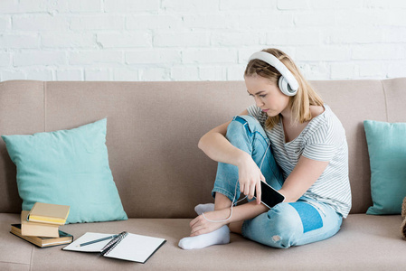 悲伤的少女坐在沙发上听音乐和耳机